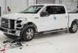 Biały pickup Ford F-150 z mocno uszkodzonym przednim zderzakiem po wypadku w centrum testowym. Na podłodze wokół samochodu widoczne są odłamki i części karoserii.